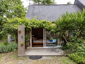 A cozy cottage with a wooden deck, a bed with patterned bedding, and a potted plant on the left. - Guesthouse 'Chambre Ailleurs' with Shared Terrace, Garden and Wi-Fi (Lannion)