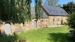 A stone building with a sloped roof and skylights, surrounded by a well-maintained lawn and trees.