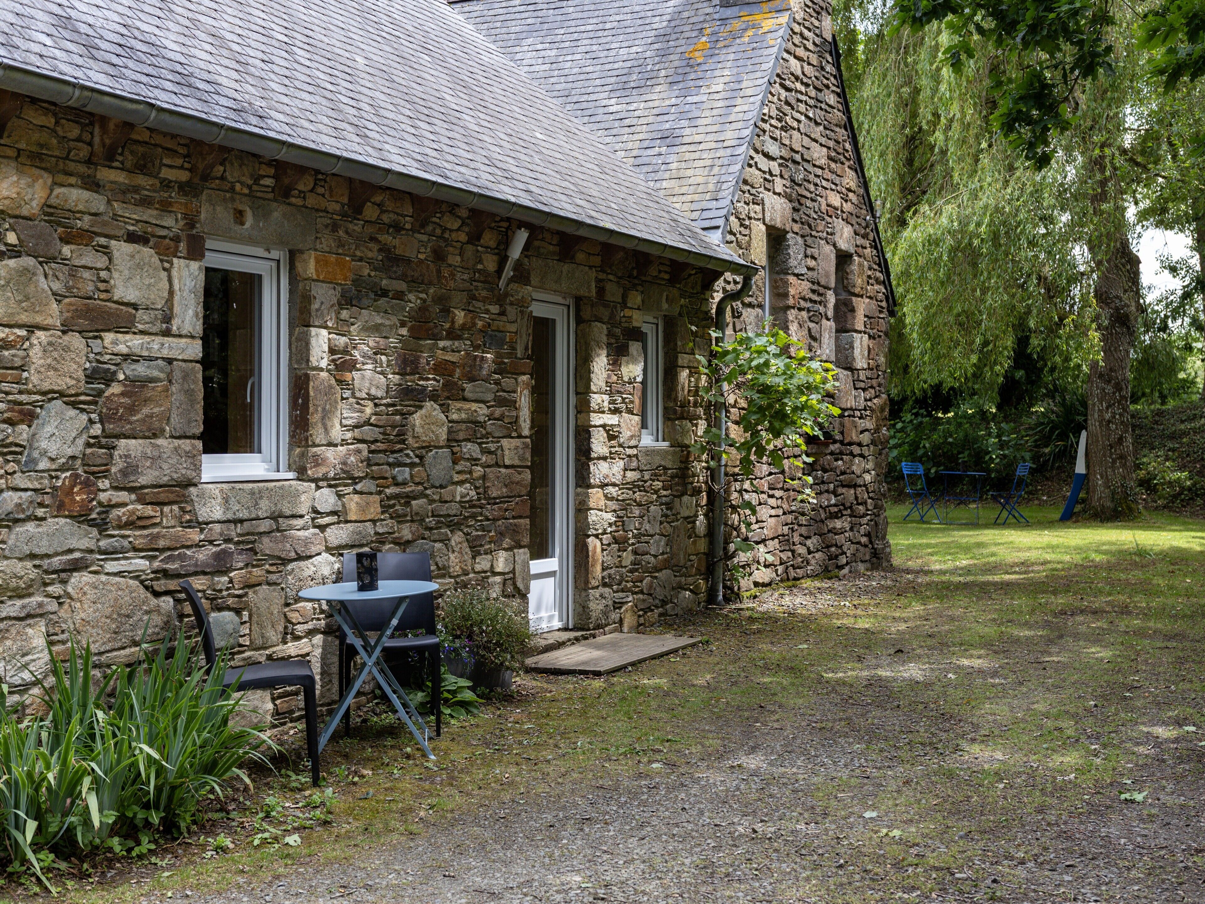 A stone building with a small patio area, a table with chairs, and a tree nearby.