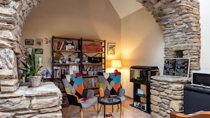 Ein gemütlicher Innenraum mit Steinwänden, einem Bücherregal, einem Tisch mit Stühlen und einem Aquarium.