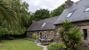 A stone house with a tiled roof, a stone pathway, and a garden with a table and chairs.
