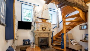 A cozy room with a fireplace, a wooden staircase, a sailboat model, and a television. - Guesthouse 'Chambre Marine' with Shared Terrace, Garden and Wi-Fi (Lannion)