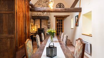 A dining area with a long table, chairs, a vase with flowers, a clock, and a fireplace.