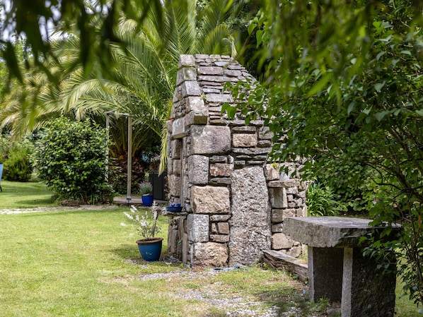Una estructura de piedra con un banco, rodeada de exuberante follaje y un césped bien cuidado.