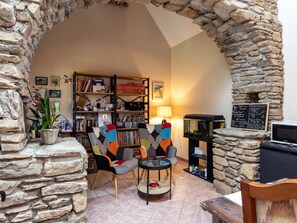 A cozy room with a stone archway, a bookshelf, a table with chairs, and a fish tank. - Guesthouse 'Petite Maison' with Shared Terrace, Garden and Wi-Fi (Lannion)