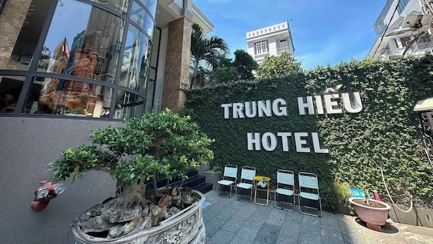 Esterno dell'Hotel Trung Hieu con un grande cartello, una facciata in vetro e una curata area giardino.