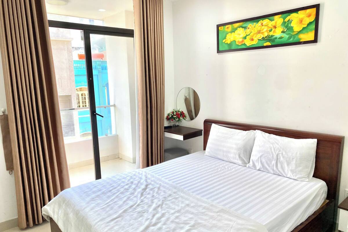 A hotel room with a bed, a desk, a mirror, and a window with curtains.