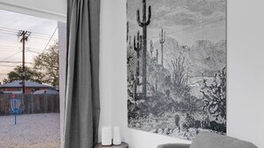 A modern living room with a grey armchair, a large black and white desert landscape painting, and a wooden side table with two white candles. - Zenergy at Sunshine Mile (Tucson)