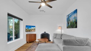 A modern living room with a grey sofa, a wooden coffee table, a fireplace, and a ceiling fan. - Zenergy at Sunshine Mile (Tucson)