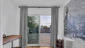 A room with a desk, a chair, a sofa, a glass door leading to an outdoor area, and a wall with a textured mural. - Zenergy at Sunshine Mile (Tucson)