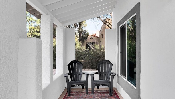 A covered patio with two chairs, a patterned rug, and a view of the surrounding area. - Zenergy at Sunshine Mile (Tucson)