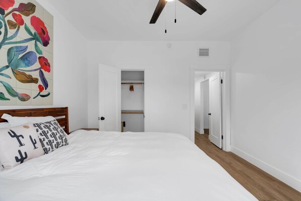 Une chambre à coucher avec un lit, une tête de lit en bois, un ventilateur de plafond et une armoire avec une porte.