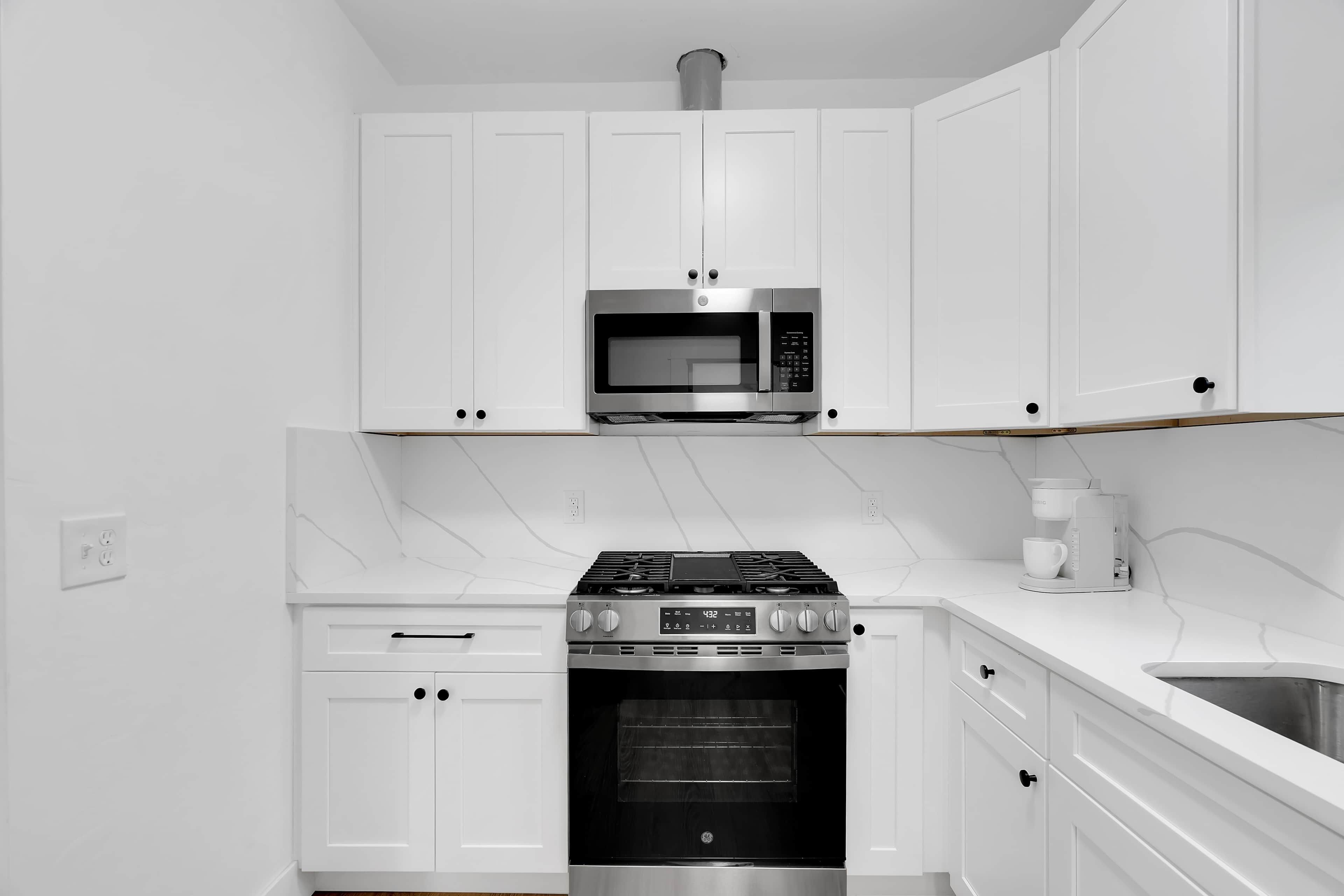 Een moderne keuken met witte kasten, een roestvrijstalen magnetron, een gasfornuis en een inbouwoven.