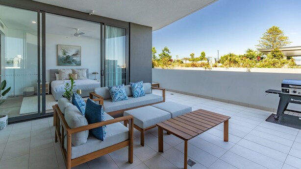 Un espacio exterior moderno con un conjunto de sofás, una mesa de madera y una parrilla.