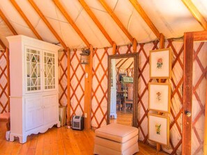 Una habitación con techo de madera, un mueble blanco, una mesita y un espejo con fotos enmarcadas.
