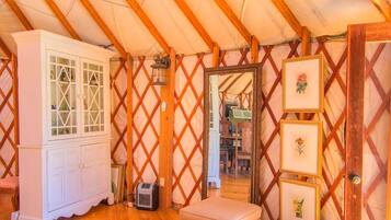 Ein Zimmer mit Holzboden, einem weißen Schrank, einem kleinen Tisch und einem Spiegel mit gerahmten Bildern.