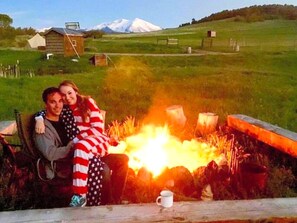 A couple sitting by a campfire with a mountainous landscape in the background.