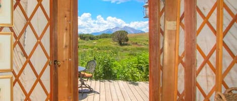 A wooden deck with a table and chair, a view of a green landscape with mountains, and a lattice door.