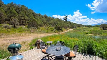 A wooden deck with outdoor furniture, a grill, and a view of a natural landscape.