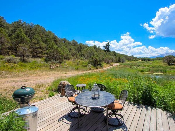 Una terraza de madera con mobiliario exterior, una parrilla y vistas a un paisaje natural.
