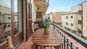 Un balcón con una mesa y sillas de madera, una planta en maceta y vistas a edificios cercanos.