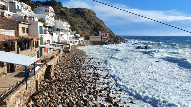 Un pueblo costero con edificios de piedra, una playa rocosa y el mar.