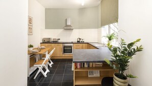 A compact kitchen with a dining area, a built-in oven, and a window with a plant. - Argyl | Central Grassmarket Apartment (Edinburgh)