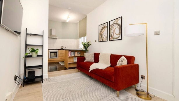 A living room with a red sofa, a white rug, a floor lamp, and a bookshelf. - Argyl | Central Grassmarket Apartment (Edinburgh)