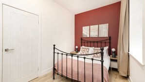 A bedroom with a bed, a nightstand, a window with curtains, and a door. - Argyl | Central Grassmarket Apartment (Edinburgh)