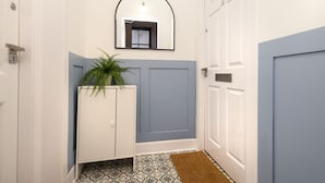 A hallway with a white door, a blue door, a white cabinet with a plant, and a patterned floor. - Argyl | Central Grassmarket Apartment (Edinburgh)