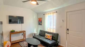 A living room with a ceiling fan, a sofa, a coffee table, a TV, and a door.