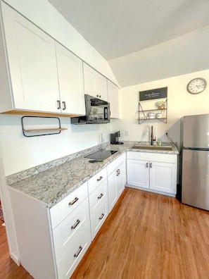 A kitchen with white cabinets, a stainless steel refrigerator, a microwave, and a clock on the wall. - Cute Casita with Stock Tank Hot Tub and Fenced Yard in Lakehills, Texas (West Lake Hills)