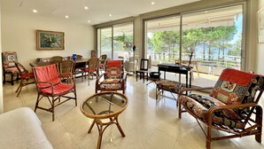 Un vaste espace de détente agrémenté de meubles en osier, d’une table à plateau en verre et de grandes fenêtres offrant une vue sur l’extérieur.