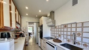 Une cuisine moderne avec des meubles blancs, une plaque de cuisson à induction noire, un évier en acier inoxydable et un crédence décorée.