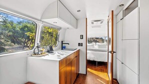 A compact kitchen with a window, wooden cabinets, and a small seating area.