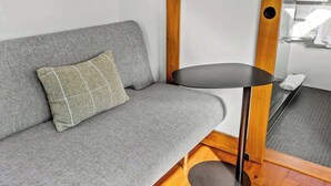 A grey sofa with a checkered pillow, a small black table with a wooden base, and a wooden floor.