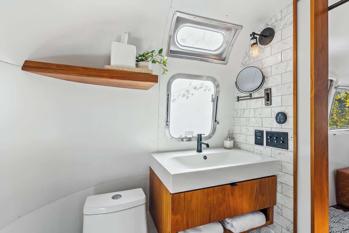 Ein kleines Badezimmer mit einem weißen Waschbecken, einem Holz-Badmöbel und einem Spiegel sowie einem kleinen Fenster.