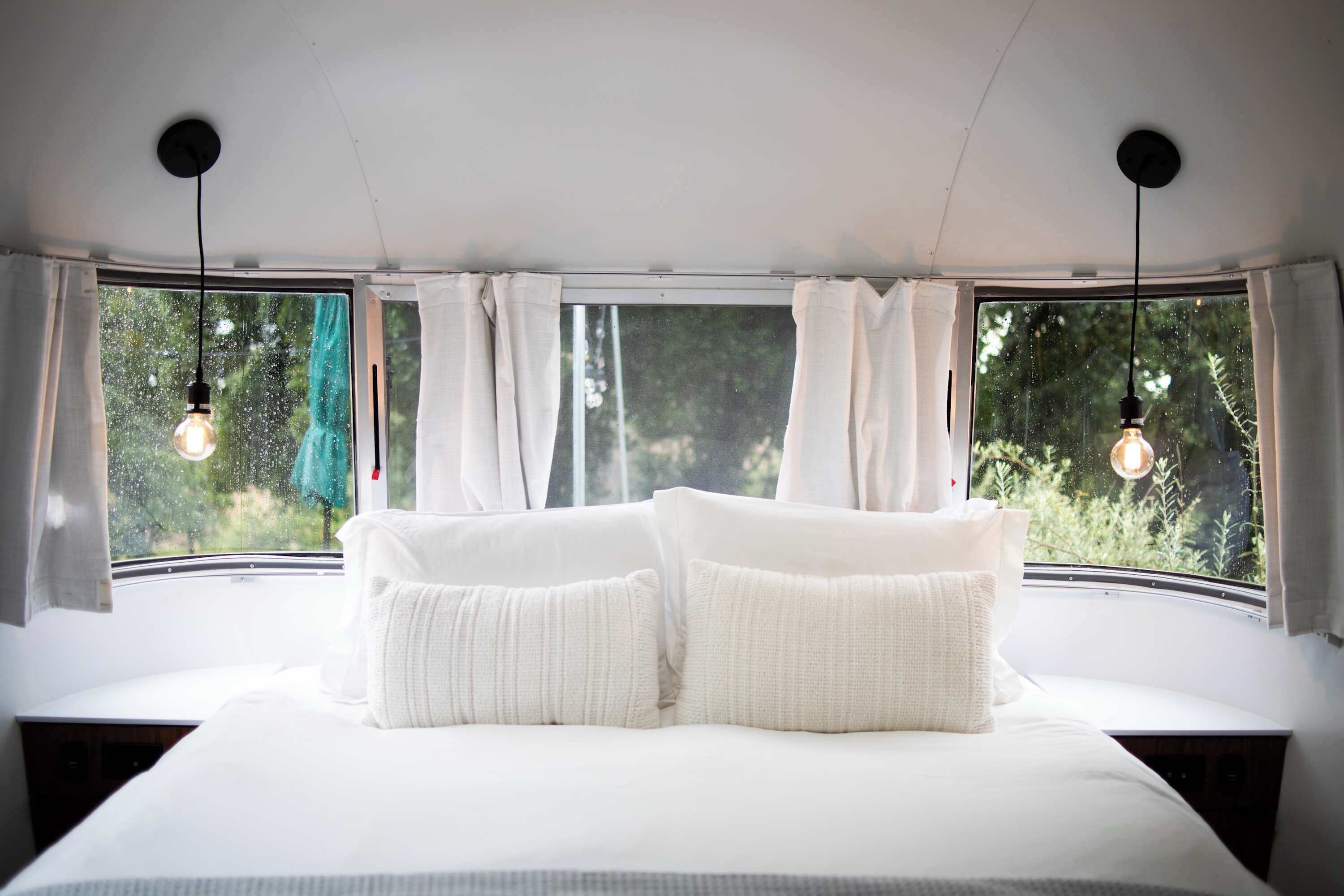 A bedroom with a large bed, white bedding, and two hanging light bulbs.