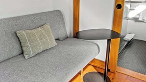 Ein graues Sofa mit einem gemusterten Kissen, ein kleiner schwarzer Tisch und Holzelemente.
