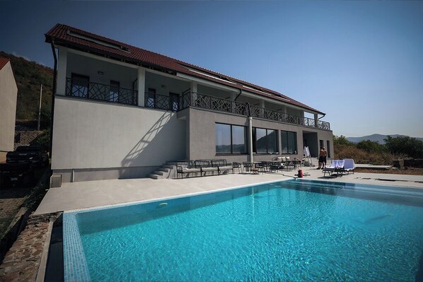 A modern building with a pool, outdoor seating, and a view of the hills. - PENSIUNEA BERZASCA (Berzasca)
