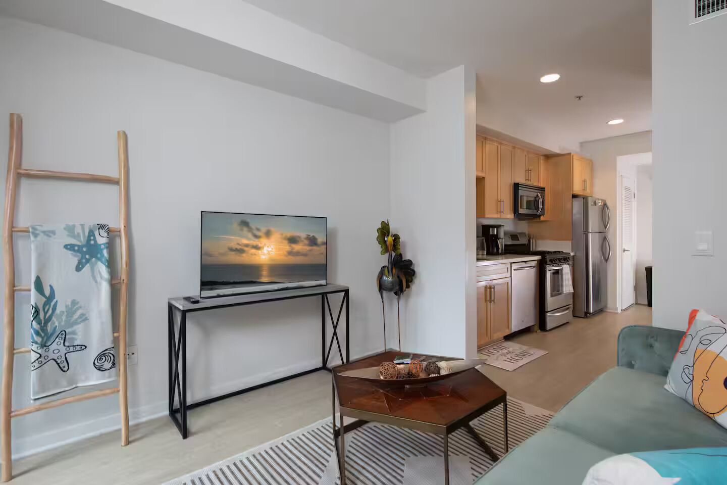 Uma sala moderna com uma TV em um móvel, uma escada de madeira, uma mesa de jantar com um vaso e uma cozinha ao fundo.
