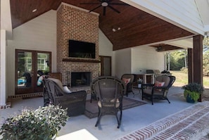 An outdoor patio with a brick fireplace, wicker furniture, and a ceiling fan.
