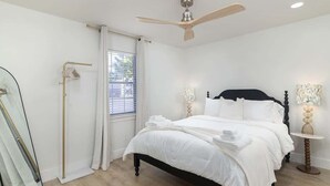A bedroom with a bed, a ceiling fan, a window with blinds, a bedside table with a lamp, and a mirror. - The Grove House (Oxford)
