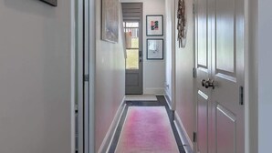 A hallway with a wooden floor, white walls, and a pink rug.