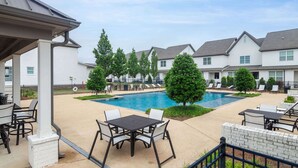 A residential area with a swimming pool, outdoor seating, and houses in the background.
