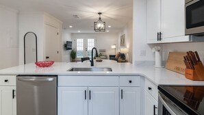 A modern kitchen with white cabinetry, a stainless steel dishwasher, a black faucet, and a wooden cutting board with knives. - The Corner at Old Taylor Place (Oxford)