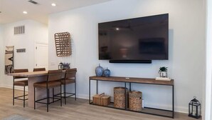 Una sala de estar moderna con una televisión de pantalla plana, una mesa de comedor de madera con sillas, una mesa consola con cestas y un televisor montado en la pared.