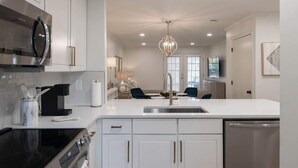 Cocina moderna con armarios blancos, electrodomésticos de acero inoxidable y una isla central con asientos.