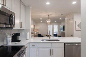 Cocina moderna con armarios blancos, electrodomésticos de acero inoxidable y una isla central con asientos.