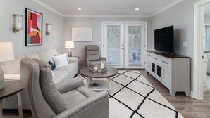 A modern living room with a sofa, armchair, coffee table, TV, and a dining area with a cabinet. - Serenity In The Sip- Walking Distance To Stadium (Oxford)